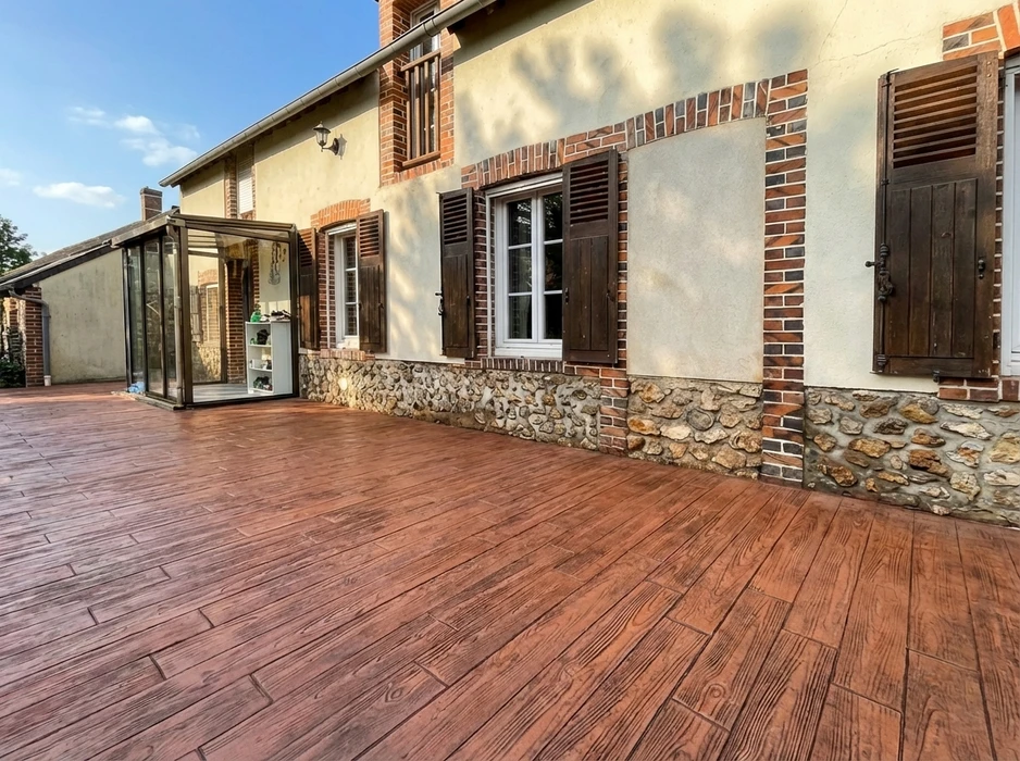 Terrasse extérieure d'une maison de style normand avec soubassement en pierres apparentes et encadrements en briques rouges