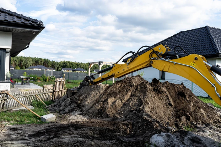 Chantier de construction extérieur avec homme en tenue de travail, casque de sécurité jaune, bras croisés devant bâtiments en construction