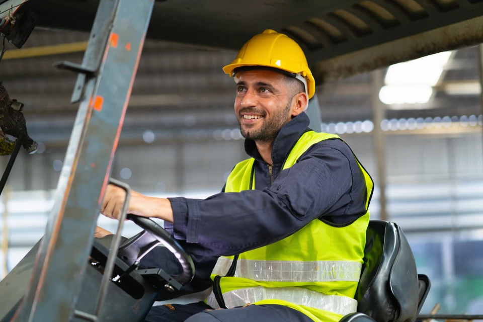 Chantier de construction extérieur avec homme en tenue de travail, casque de sécurité jaune, bras croisés devant bâtiments en construction