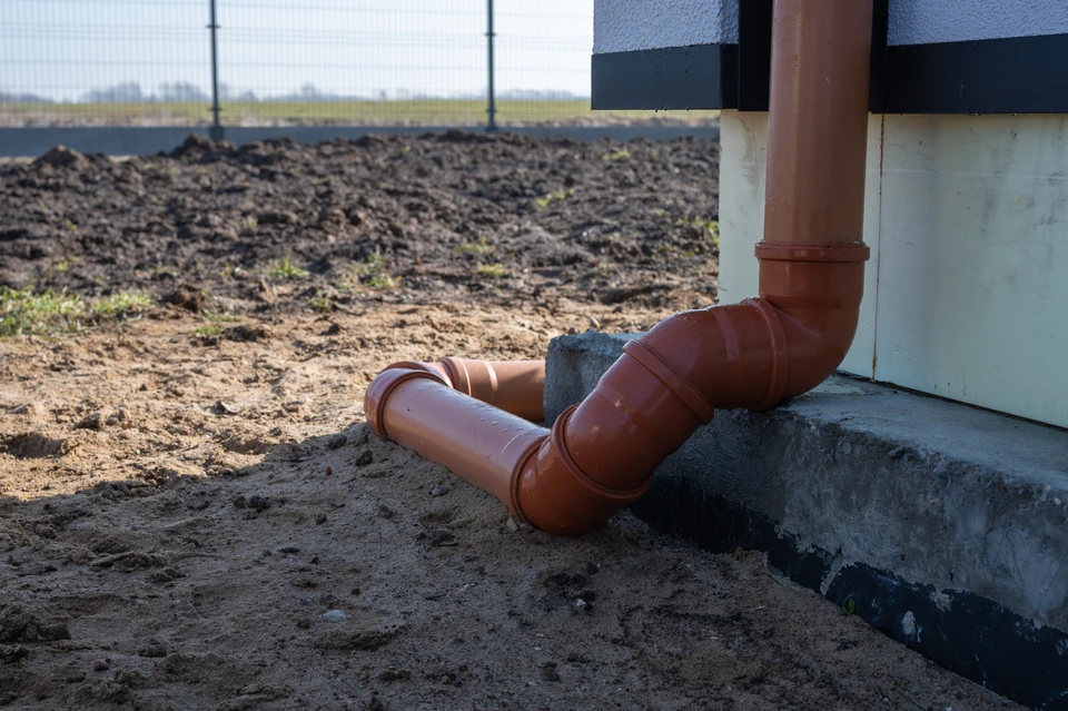 Scène extérieure sur terrain de terre, mains d'ouvrier en gants de protection gris manipulant un outil de serrage sur raccordement de canalisation